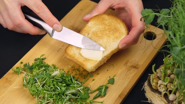 Spreading soft butter on a slice of bread. Spreading cream cheese on bread. making a healthy breakfast with sprouted micro greens.