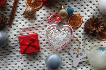 Various colorful Christmas ornaments, small presents and seasonal spices on white knitted blanket. Top view.