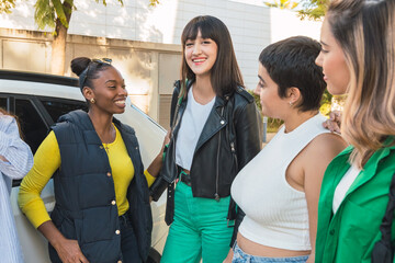 Happy ethnic young woman standing with diverse friends near car in daylight
