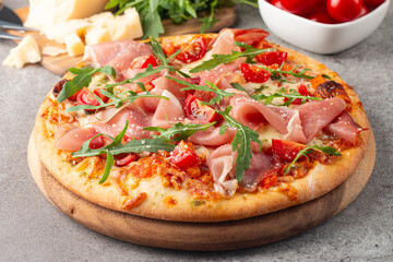 Pizza with prosciutto, ham, arugula, tomatoes, pesto, cheese and parmesan. Italian cuisine. 