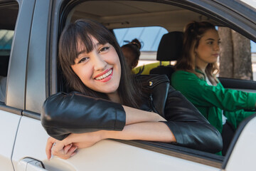 Cheerful ethnic woman sitting in parked white car near tree trunk