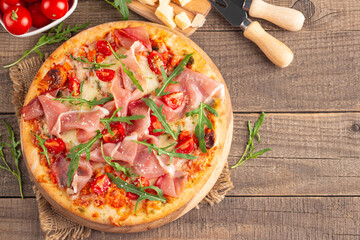 Pizza with prosciutto, ham, arugula, tomatoes, pesto, cheese and parmesan. Italian cuisine. 