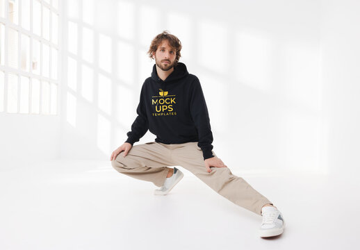 Mockup of man wearing customizable hoodie crouching in studio, leg out