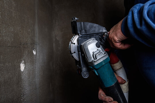 Worker holding angle grinder with two diamond discs for cutting grooves in wall.