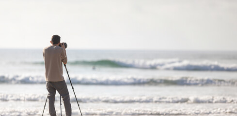 Young handsome photographer with a tripod and a camera on the beach - Powered by Adobe