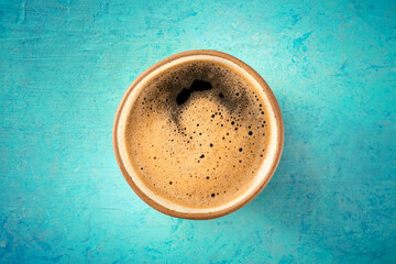 A cup of black coffee with froth, a close-up, overhead flat lay shot on a blue background