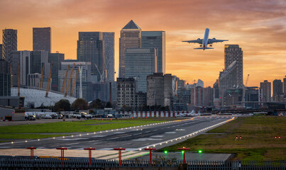 Panoramic view of the London skyline with Canary Wharf district and the runway of the City Airport in front during sunset time