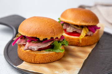 hot burgers with lettuce and vegetables on a wooden board side view