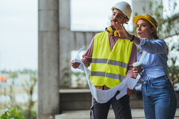 Young woman architect explaining blueprint to supervisor wearing safety vest at construction site....