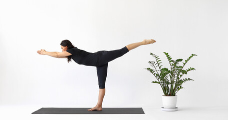 Yoga instructor performing Virabhadrasana exercise, warrior number three pose, working out in short leggings and a T-shirt, standing on a mat in the studio