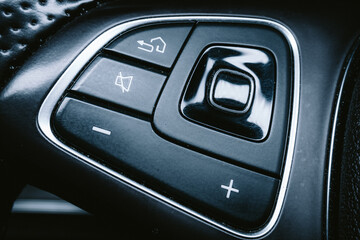 Modern car steering wheel with buttons and switches. Close up shot, perforated leather wrapped, no...