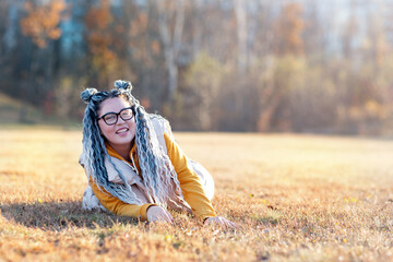 a cheerful girl with dreadlocks and glasses is lying in an autumn meadow