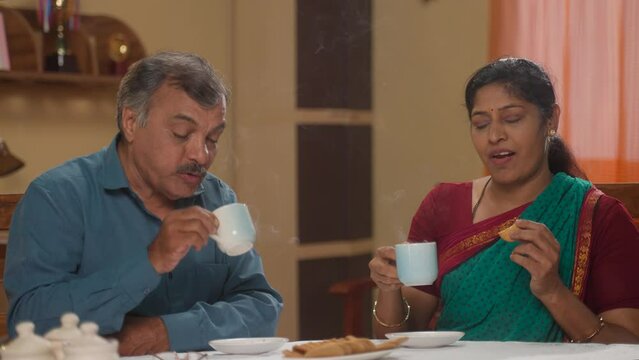Indian senior couples enjoying morning tea and biscuits at home - concept of healthy morning routine, refreshment and retirement lifestyle