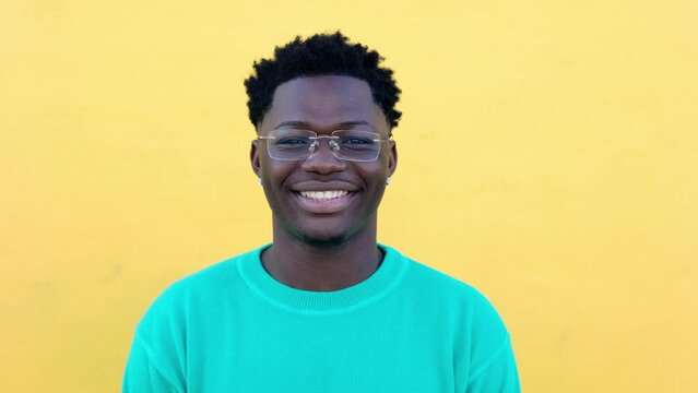 Close-up portrait of young adult african man smiling at camera over yellow background. Front view headshot of joyful black guy feeling positive outdoors.