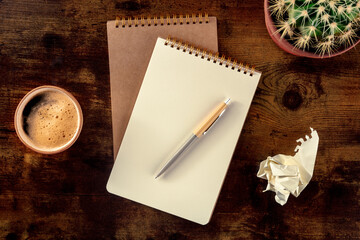 Notebook with a pen, coffee, and plant, overhead flat lay shot on a rustic wooden desk, with a...