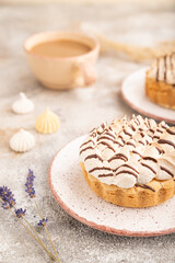 Two tartlets with meringue cream and cup of coffee on brown concrete, side view, selective focus.