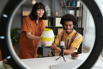 Happy young intercultural bloggers showing handmade items to their audience