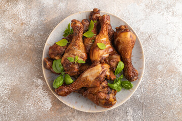 Smoked chicken legs on a ceramic plate on a brown concrete background. Top view, close up.