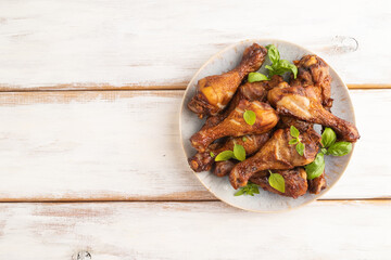 Smoked chicken legs on a ceramic plate on a white wooden background. Top view, copy space.