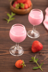 Sweet strawberry liqueur in glass on a brown wooden background. side view, selective focus