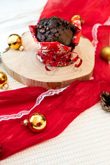 Brown muffin on a plate with a festive red ribbon. The golden Christmas ornaments scattered on the ribbon add a touch of opulence. Warm tones of the muffin harmonize with the vibrant red and gold