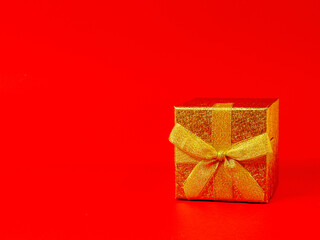 golden gift box with a bow lying on its side with the lid in front on a red background