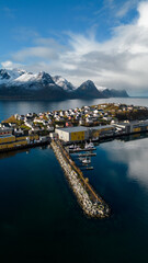 Aerial of a small island fishing town of Husoy on Senja, Norway.  A fishing village located in the Arctic Circle of Northern Norway.  Shot with a drone at the fishing pier showing many boats docked.