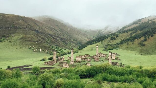 View of the medieval Targim tower complex in the Caucasus mountains surrounded by greenery. The Caucasus Mountains on a cloudy day in Ingushetia. Russia, 4K.