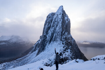 Hiker climbing snowy mountain hike up Segla in Senja, Norway.  A man walking up snowcapped mountains in the Arctic Circle of Northern Norway.  Famous hike on Senja island.  Shot in October - obrazy, fototapety, plakaty