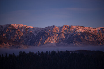 Winter landscape with high and snowy rocky mountains. Amazing sunset in shades of purple in the...