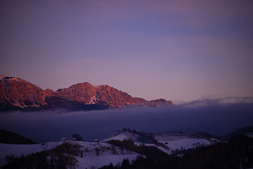 Winter landscape with high and snowy rocky mountains. Amazing sunset in shades of purple in the evening sky