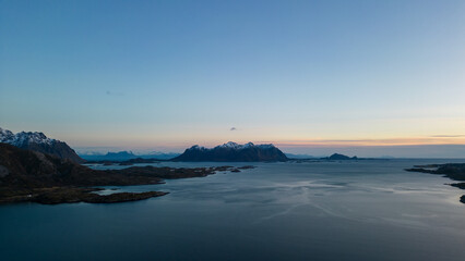 Aerial of highway along fjords in Lofoten, Norway at sunset.  Snow covered mountains captured on image by a drone.  Located far North in the Arctic Circle.