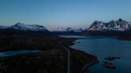 Aerial of highway along fjords in Lofoten, Norway at sunset.  Snow covered mountains captured on image by a drone.  Located far North in the Arctic Circle.