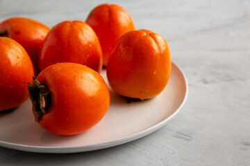 Organic Persimmon Fruit on a Plate on a gray background, low angle view. Copy space.