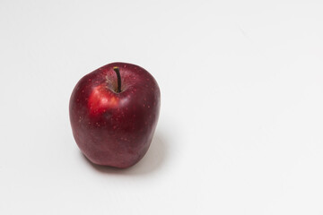 A whole red apple on a white table with a white background.