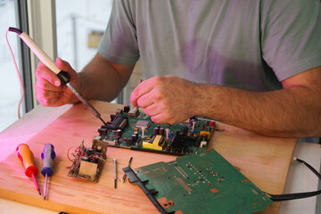 A man holds a soldering iron in his hand and solders a microcircuit