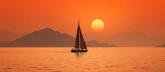 Rolgordijnen A sailboat with raised sails is outlined against the sunset and hazy orange sky amidst two coastal landmasses in Costa Rica copy space image © vxnaghiyev