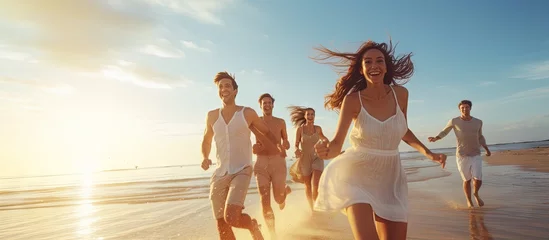 Fototapeten Attractive young friends running and smiling on beach having fun copy space image © vxnaghiyev