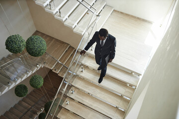 High angle shot of African American businessman wearing suit carrying laptop descending stairs...