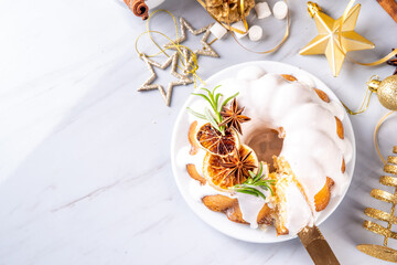 Christmas bundt cake decorated with sugar icing, orange and rosemary. Traditional Christmas and New Year baked dessert, vanilla sponge fruit cake, in white xmas decorated background