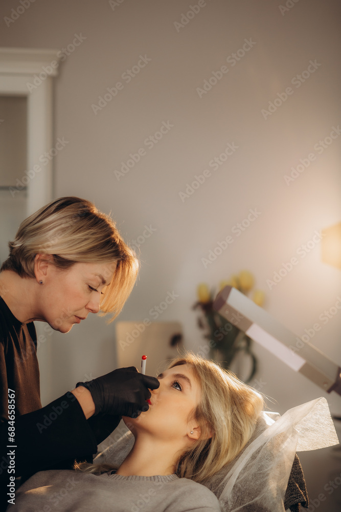 Wall mural amazing brunette woman having lip permanent procedure at the beauty studio.