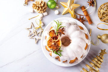 Christmas bundt cake decorated with sugar icing, orange and rosemary. Traditional Christmas and New Year baked dessert, vanilla sponge fruit cake, in white xmas decorated background