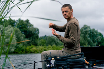 Portrait of a serious fisherman stringing a bait on the hook of a fishing rod for catching river fish