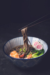 Japanese Soba noodle soup with shrimp tempura or Nabeyaki udon on the dark rustic background....