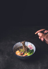 Japanese Soba noodle soup with shrimp tempura or Nabeyaki udon on the dark rustic background. Tagliatelle made from buckwheat flour, winter food.  Male hand with chopsticks takes soba, front view
- 684661957
