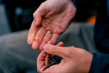 Close-up male fisherman's hand stringing bait onto the hook of a fishing rod for catching river fish