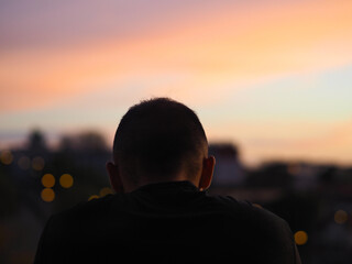 Jeune homme de dos à son balcon observant le coucher de soleil