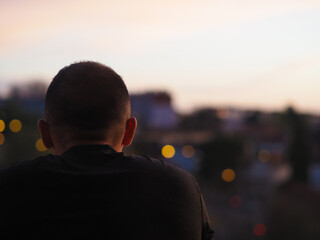 Jeune homme de dos à son balcon observant le coucher de soleil