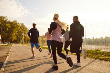 Several athletes having outdoor jogging workout. Back view from behind group of five people in sportswear and sports shoes running on city street on sunny summer morning. Exercise, fitness concept