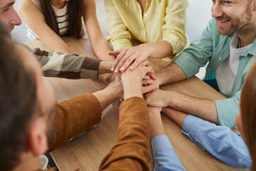 Team of friends stacking hands. Group of happy, smiling young people sitting together around a...